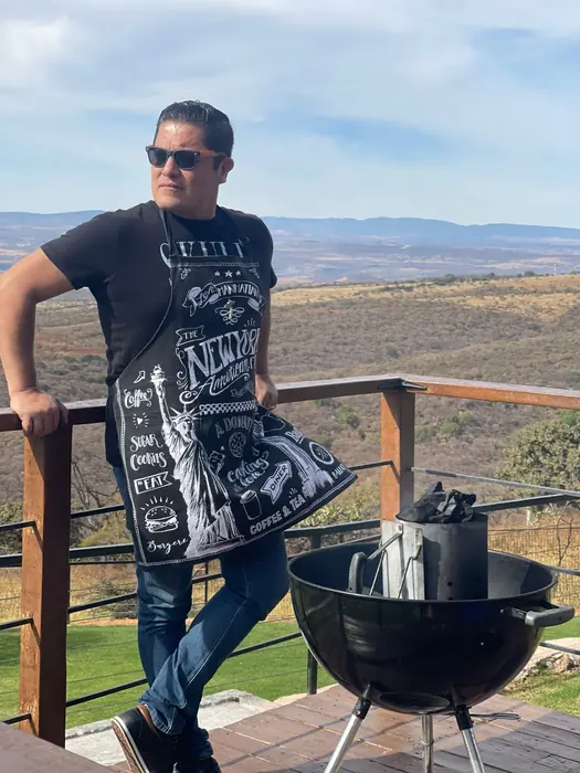 Maestro parrillero con mandil junto a un asador